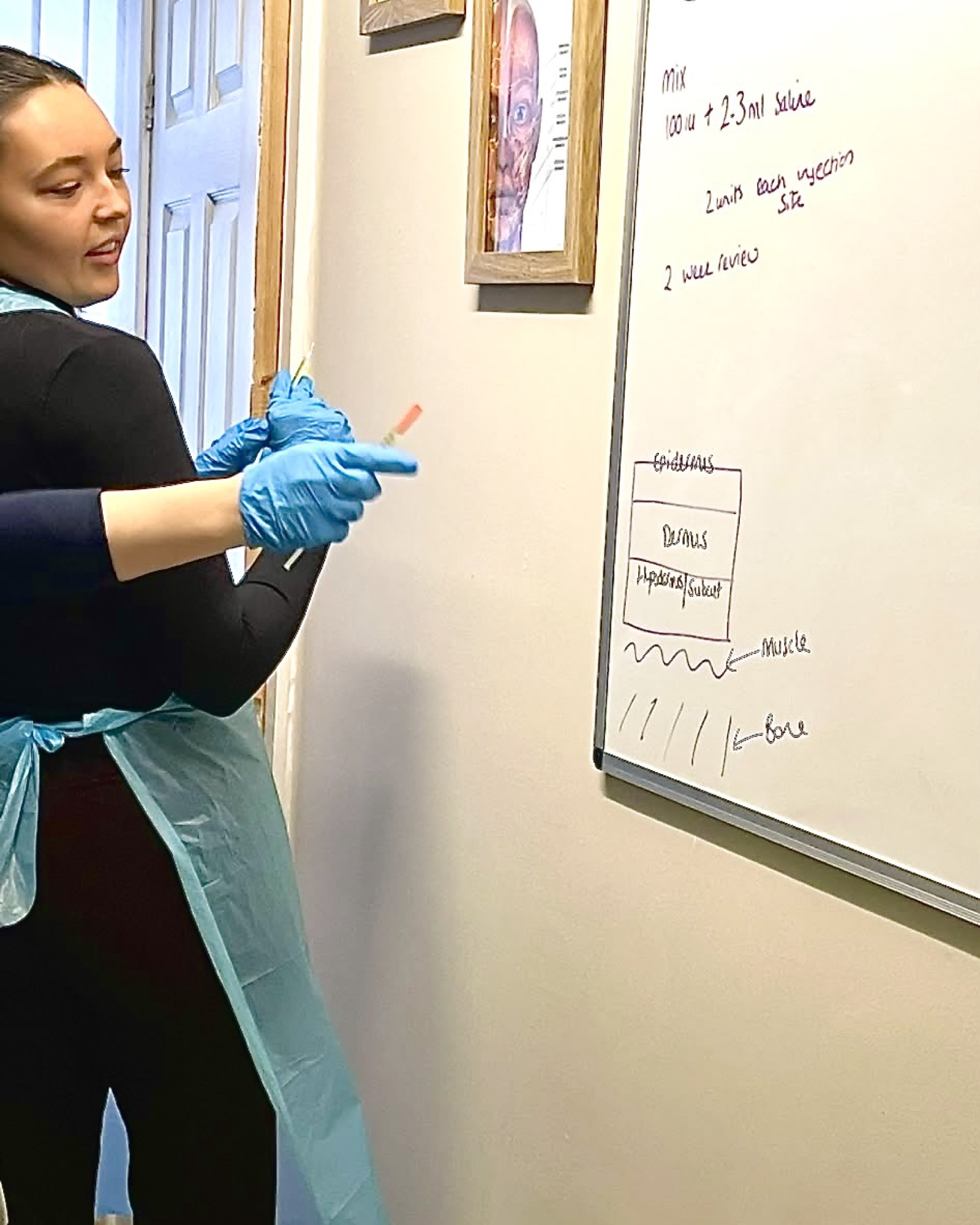 Practitioner in protective gloves preparing treatment materials beside a clinical whiteboard.