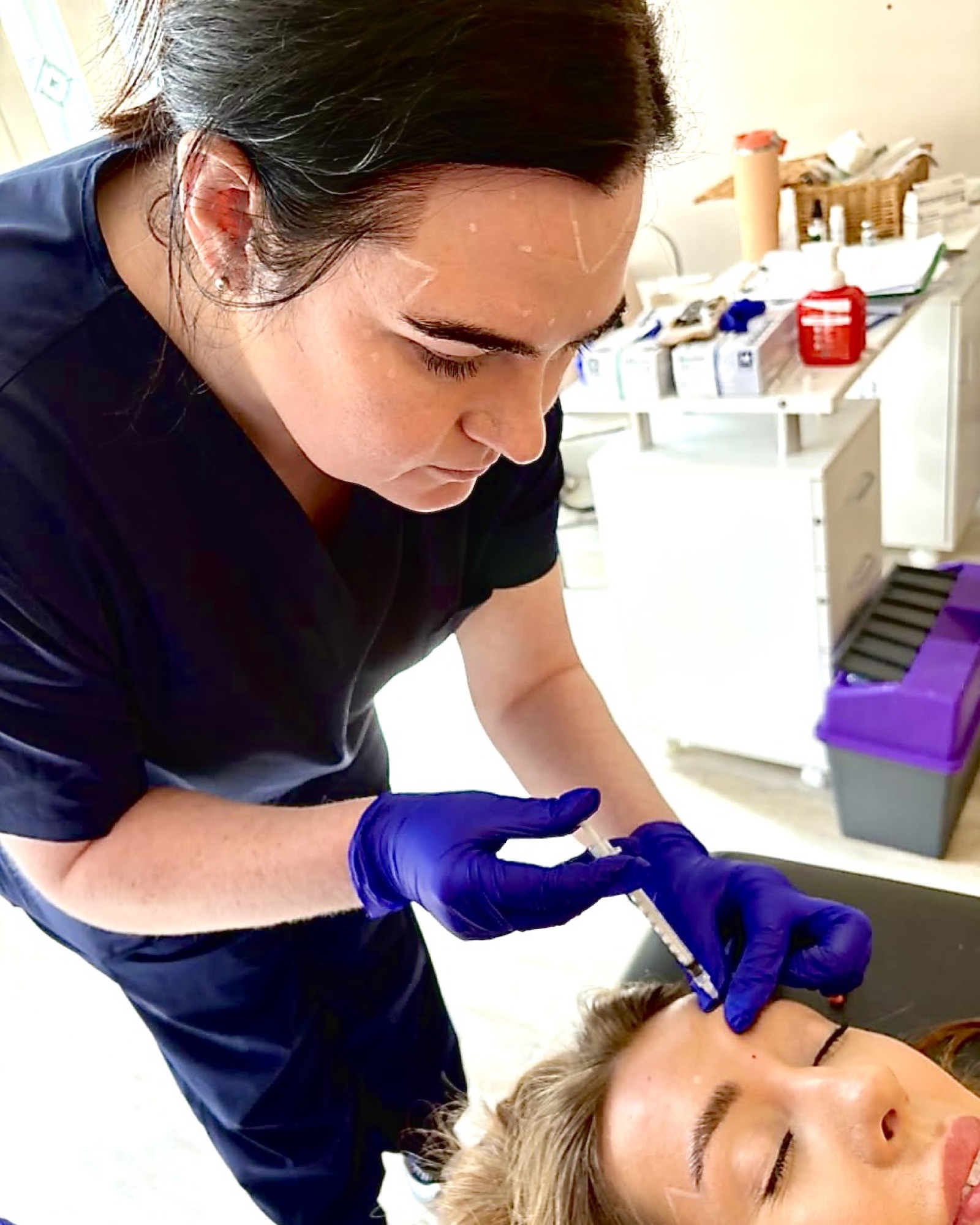 Practitioner in blue gloves demonstrating an injectable treatment technique on a client.
