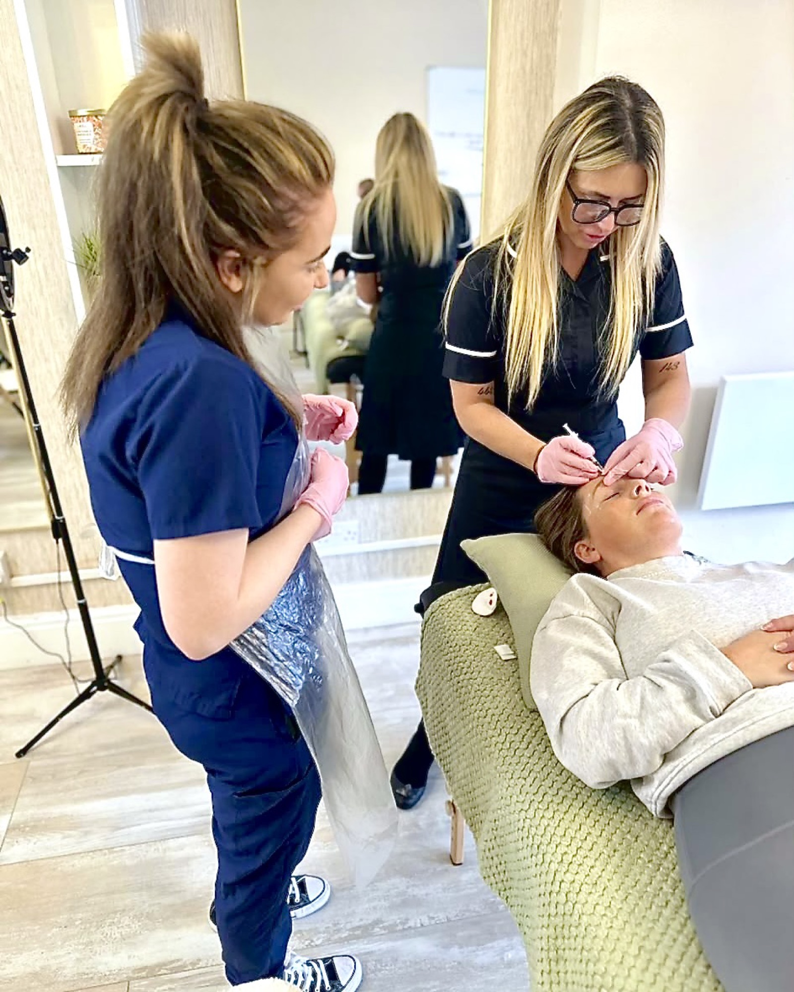 Two practitioners in scrubs performing a supervised treatment on a reclining client.
