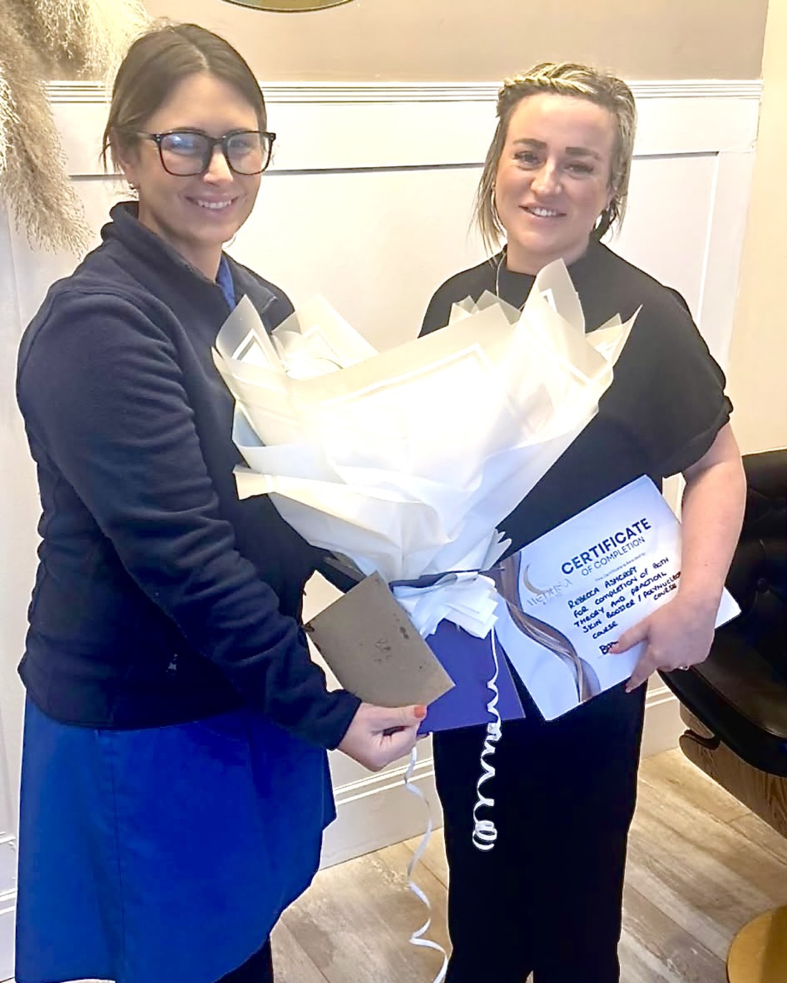 Training Example - Clinical Achievement Two practitioners holding flowers and a clinical training certificate.