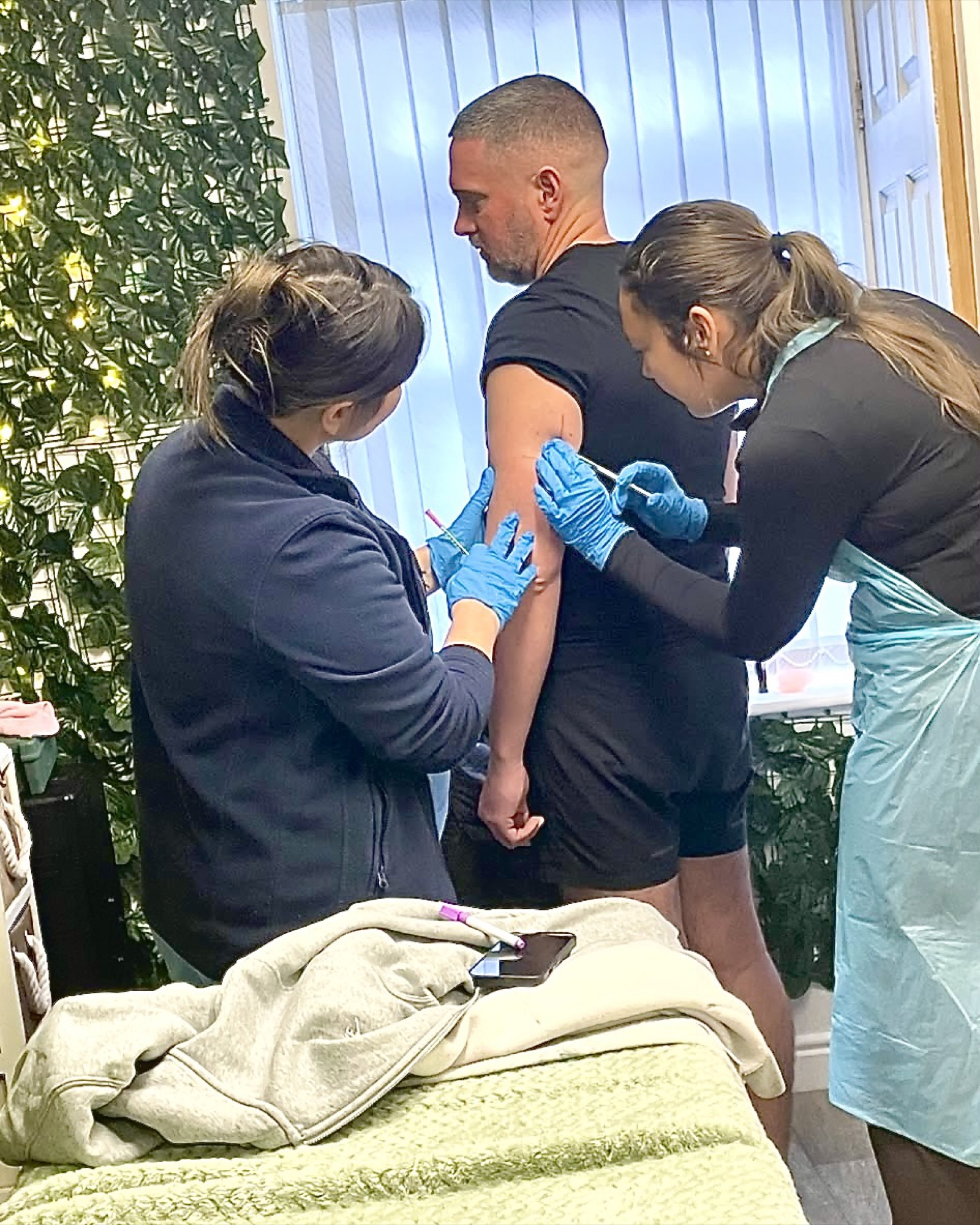 Three practitioners in protective gloves practising an injection procedure on a training model.